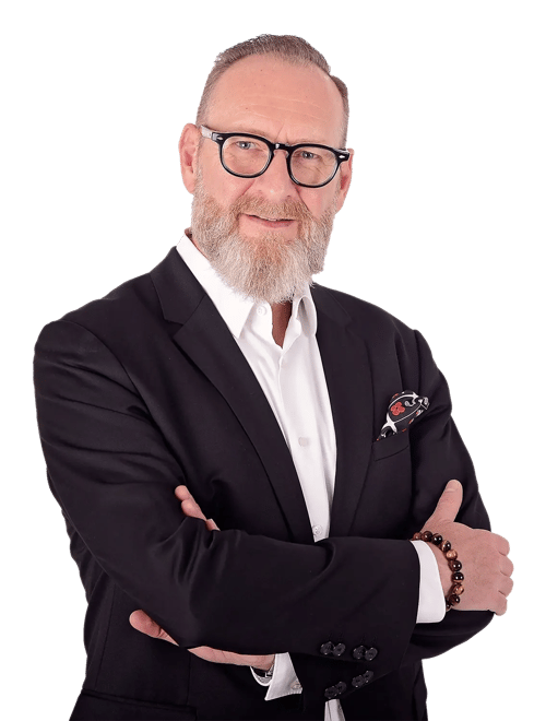 Business-Porträt vor transparentem Hintergrund. Oliver Burgdorf Mitarbeiter von RIEDEL Networks trägt ein schwarzes Sakko über einem weißen Hemd, mit einem gemusterten Einstecktuch. Die Arme sind vor der Brust verschränkt, am Handgelenk ist ein Armband sichtbar.